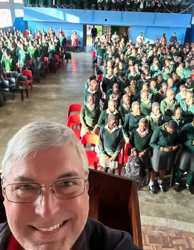 Man taking selfie at large dental conference or gathering with hundreds of attendees in green shirts.