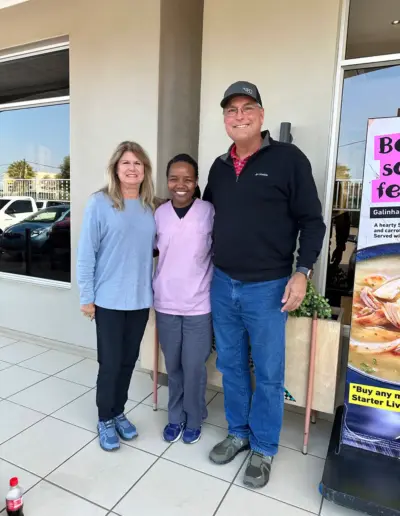 Three people smiling inside a dental office lobby with promotional signage visible.