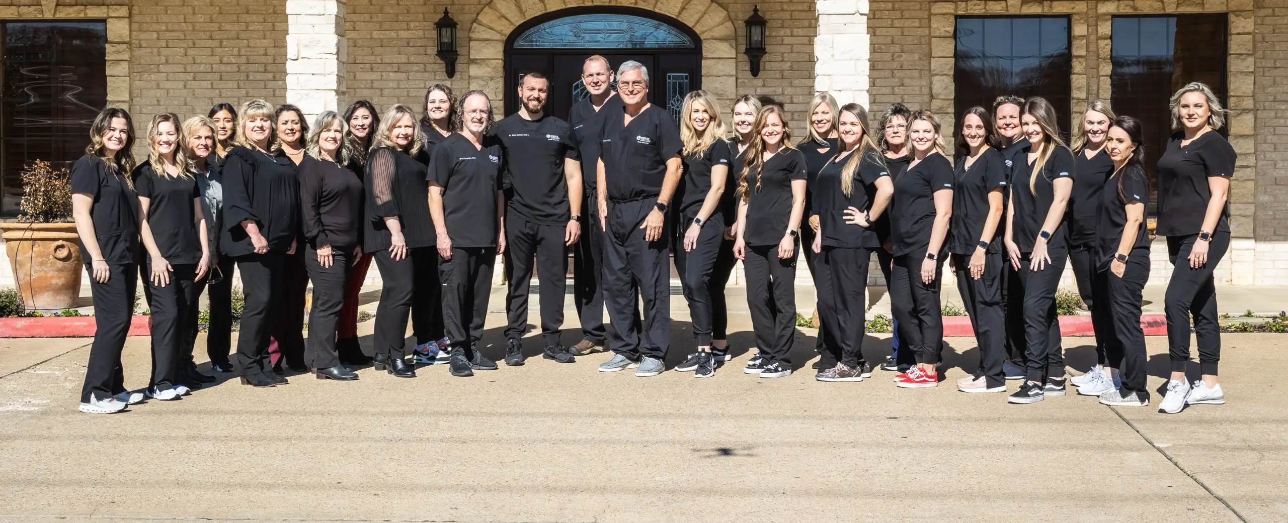 Legacy Dental Group team standing together in professional black attire outside brick building.